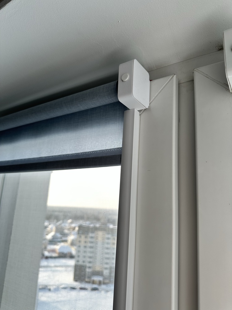 Small white motorized roller blind box mounted above a window