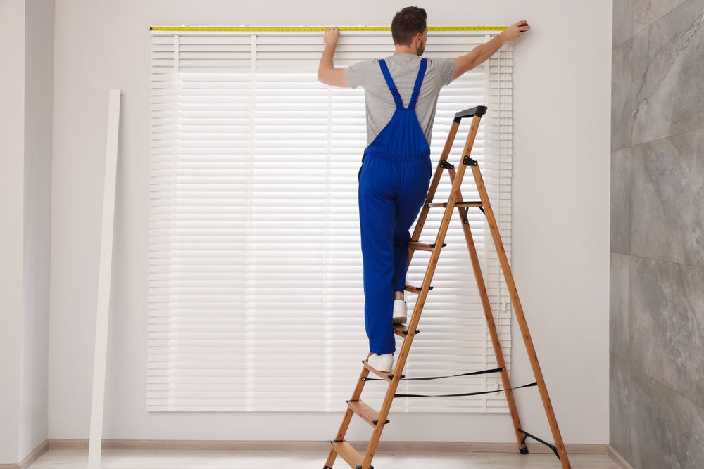 Worker using measuring tape while preparing to install window blinds